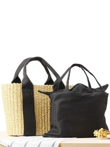 Minimalist beige woven straw tote bag with black fabric handles and inner pouch on wooden desk