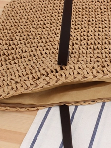 Handmade woven straw tote bag with brown leather straps and metal zipper on wooden table