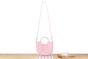Detail of pink woven half-moon bag with circular handle and detachable strap on wood
