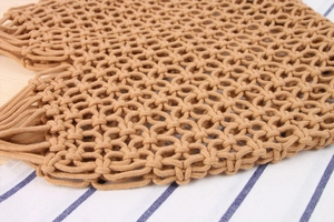 Close-up of hand-woven macrame grid texture with bohemian tassel details on a brown bag