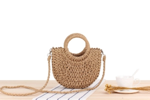 Detail of a beige semi-circular woven straw bag with ring handle and a long shoulder strap
