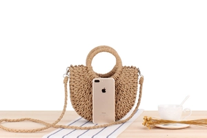 Detail of hand-woven semi-circle straw bag with round handles and a detachable shoulder strap