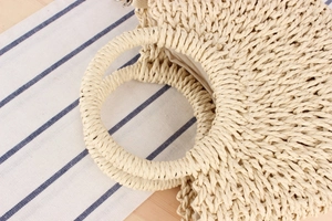 Detail of woven straw handbag showing the round handle and beige fabric lining texture