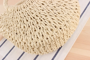 Close-up of beige woven straw handbag featuring a round handle on a striped fabric