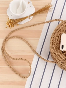 Handwoven round straw shoulder bag on a minimalist wooden table with vacation vibes