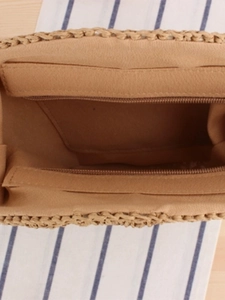 Internal view of beige woven round straw bag with fabric lining and secure zipper pocket