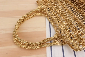 Détail du sac de plage doré tissé à la main avec poignées torsadées sur une table
