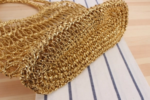 Détail du sac de plage tissé doré montrant la texture crochetée sur une surface en bois