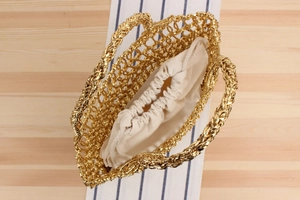Détail d'un sac à main tissé doré avec doublure à cordon beige sur une surface en bois