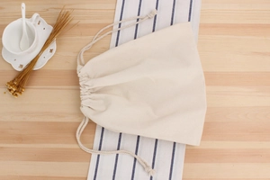 Détail d'un sac à cordon en coton naturel avec texture sur une table en bois épurée