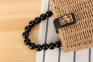 Détail du sac en paille tressée avec poignées en perles noires et fermoir doré