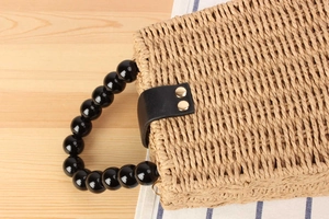 Détail du sac en paille avec anse en perles noires et rivets métalliques dorés sur cuir