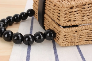 Détail du sac en paille tressée avec anse en grosses perles de bois noires et brillantes