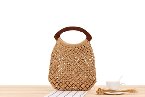Close-up of handmade cotton rope woven beach bag with round wooden handles on wooden desk