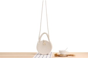 Detail of round beige woven cotton rope crossbody bag with wooden buckle on table