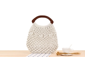 Detail of macrame woven cotton beach bag with circular dark brown wooden handles