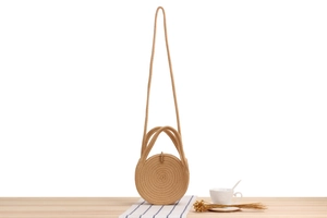 Close-up of a khaki woven round bag with spiral texture on a wooden desk with props