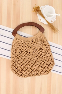 Detail of macrame beach bag with hollow weave patterns and dark brown wooden handles