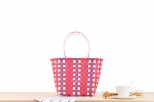 Detail of colorful woven tote bag with pink, blue stripes and white handles on table