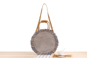 Detail of a paper rope woven round bag featuring blue fringes and a leather shoulder strap