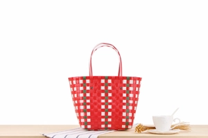 Detailed close-up of a red and green plaid woven beach bag on a wooden table