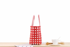 Detail of red and white checkered woven basket bag on a wooden table with decor