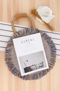 Detail of round straw bag with blue fringes, leather handle on a minimalist table