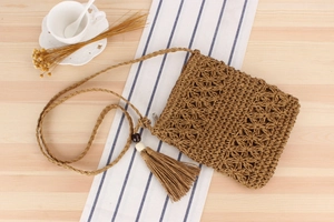 Detail of hand-woven hollow straw bag with fringe tassel and wood beads on a table