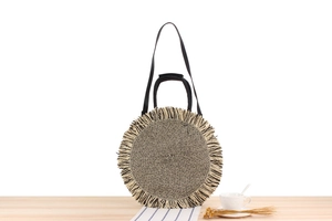 Detail of round paper rope woven bag with bicolor fringe and black handles