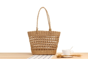 Detail of handmade woven straw tote bag with hollow mesh design on a wooden desk