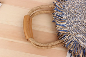 Macro detail of the woven paper straw bag featuring blue fringe and leather handle grip