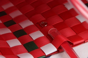 Close-up of woven tote showing metal rivet hardware and clear plastic handle detail