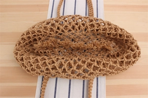 Détail d'un sac cabas en maille tissé main avec franges sur un fond en bois rustique