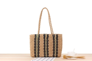 Vertical striped straw tote bag placed on a wooden table with a coffee cup and dried flowers