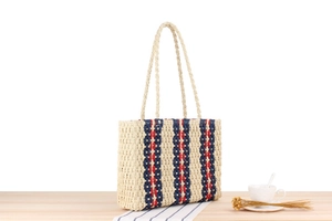 Detailed view of striped paper rope woven beach bag on a light wood surface with accessories