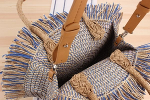Detail of woven straw bag with blue wave pattern, leather handles and fringe trim