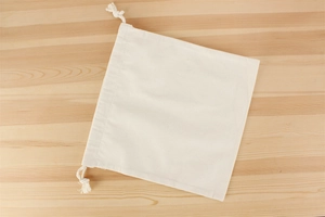 Detail view of a natural canvas drawstring inner bag for woven handbags on a wooden surface