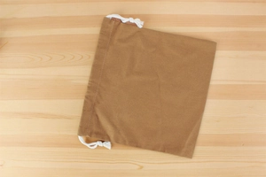Detailed view of a brown canvas drawstring inner bag on a light wood grain surface