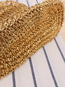 Sac fourre-tout en maille dorée tressée posé sur un tissu à rayures bleues élégant