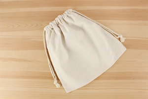 Close-up of cream canvas drawstring inner bag with woven texture on wood surface