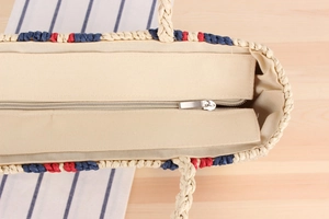 Detailed close-up of woven paper rope beach bag featuring secure silver metal zipper closure