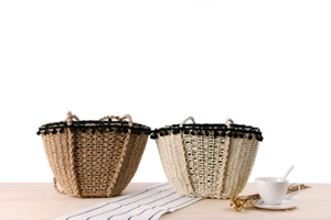 Detail of woven straw beach bag with black pom-pom trim and rustic wood handle