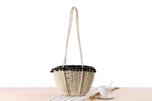 Close-up of beige straw beach tote featuring black pom-pom trim and open weave detail