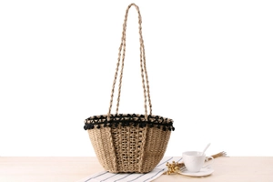 Detail of woven straw beach bag featuring black pom-pom trim and rustic textures