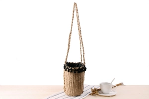Detail of hand-woven straw bucket bag featuring black lace trim and pompom accents