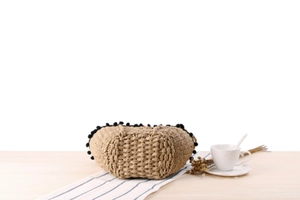 Detail view of straw woven beach bag with black pom-pom accents on a wooden table