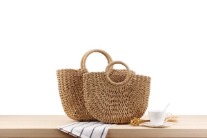 Detail of natural woven paper rope handbags with circular handles on a wooden table