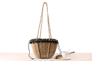 Detailed close-up of woven paper straw bag with black pom-pom lace and shoulder strap