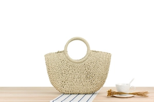 Detail view of woven straw tote bag on wooden table with dried flowers and coffee cup