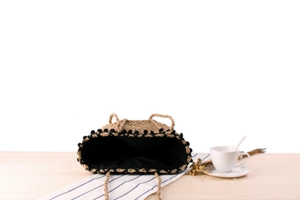 Detail of straw beach bag with black pom-pom trim and spacious interior lining